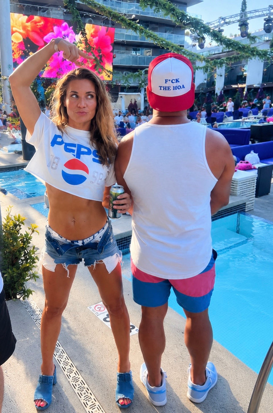 Customer pointing to a red F*ck the HOA hat at a poolside gathering